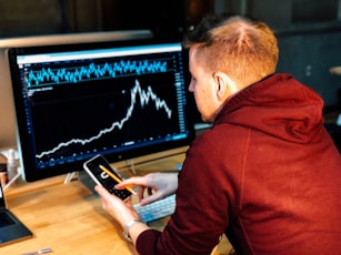 man holding black smartphone with flat screen monitor in front