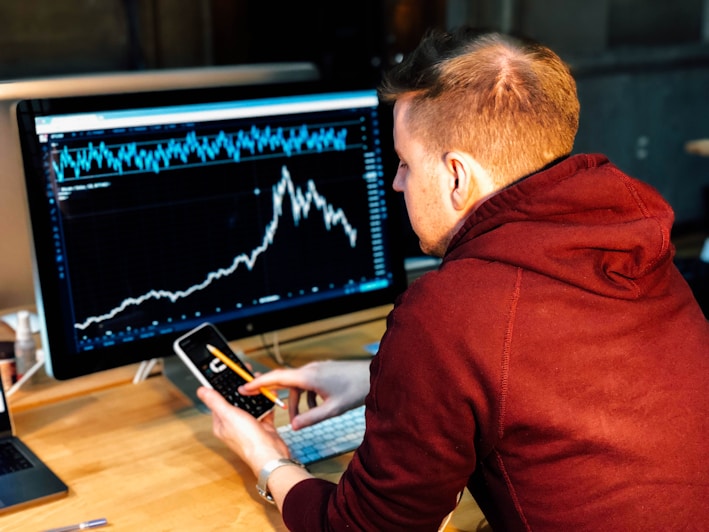 man holding black smartphone with flat screen monitor in front