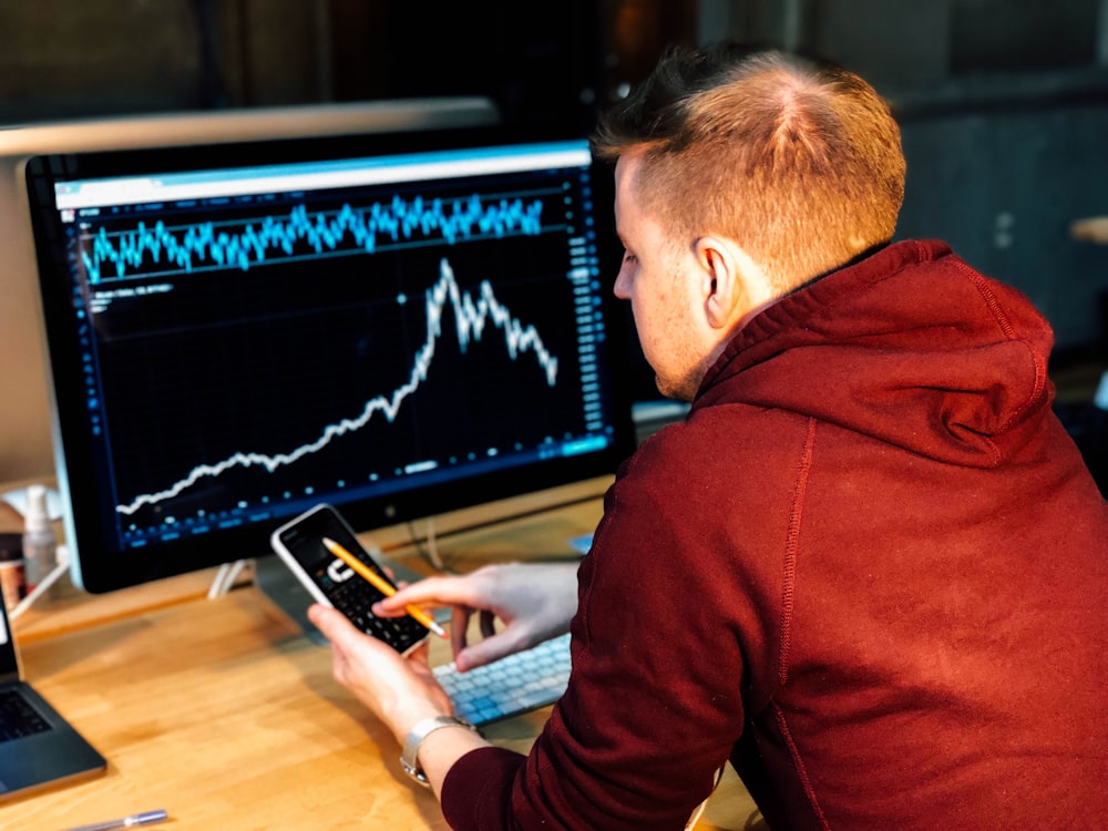 homem segurando smartphone preto com monitor de tela plana na frente