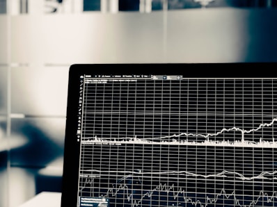 A computer screen displays a detailed financial graph with multiple lines and grids, indicating market trends over time. The background is blurred, giving focus to the graph.