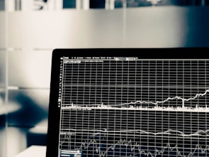 A computer screen displays a detailed financial graph with multiple lines and grids, indicating market trends over time. The background is blurred, giving focus to the graph.