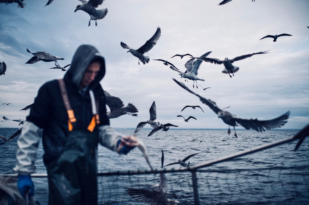 man wearing black waders beside rail near flock of birds