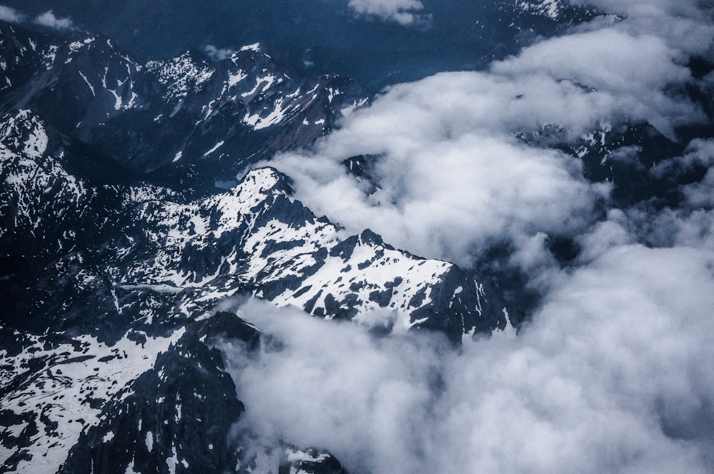 aerial photo of white clouds above gray mountain covered with snow at daytime
