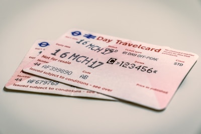 Two travel tickets are placed on a flat surface. The tickets are for a day pass, with printed text showing details like the date, type of travel, and zones. The predominant color of the tickets is a light pink, with black text and some blue and red symbols.