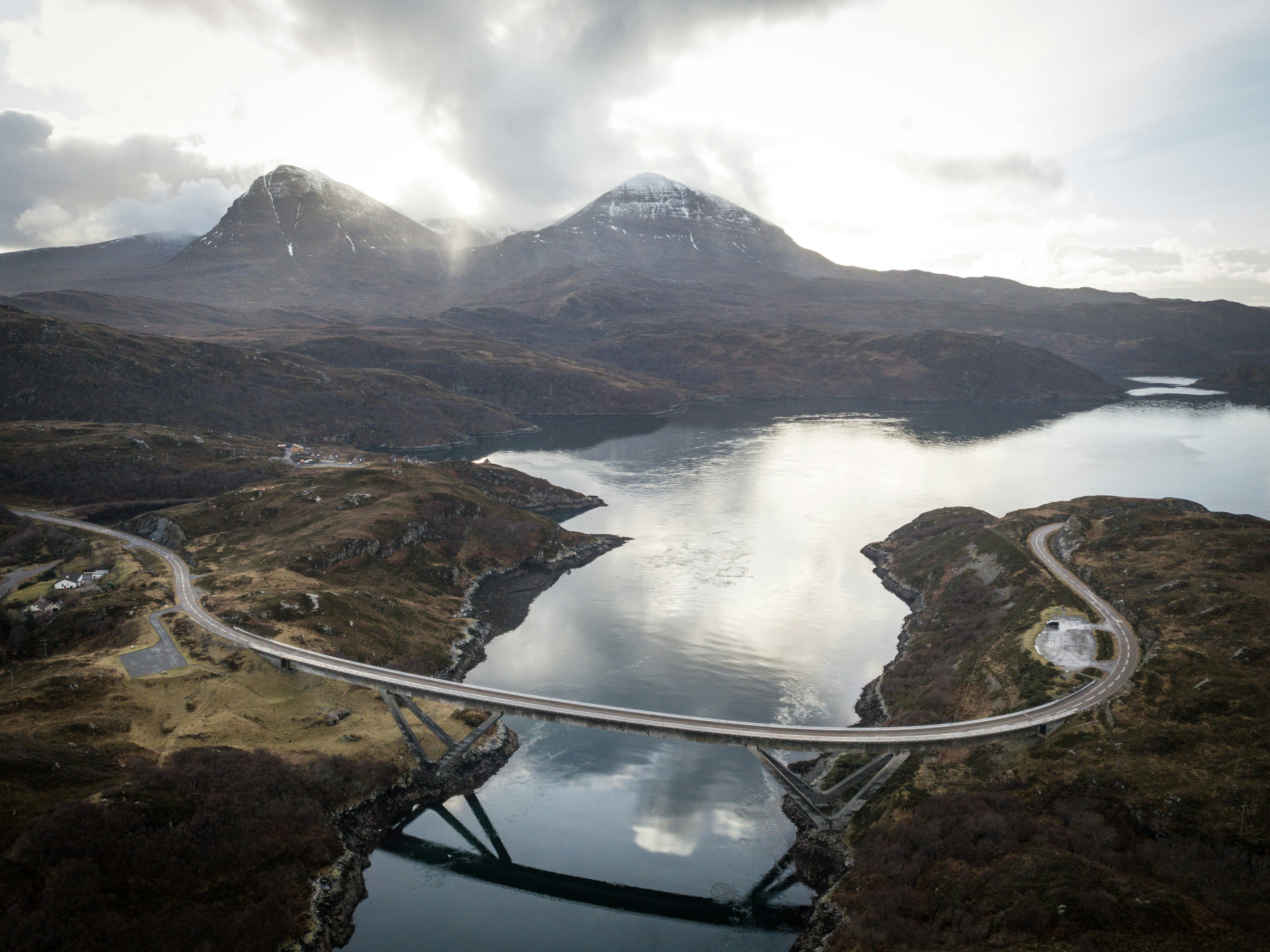 concrete road bridge near two snow-capped mountains during daytime