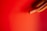 A hot dog protrudes from the right side against a vibrant red background. The hot dog is nestled inside a sliced bun, with a glossy sheen on the sausage.