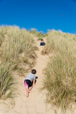 Children playing near an ochre-colored sandy path under bright blue skies.
