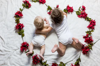 two baby's lying surrounded by red petaled flowers