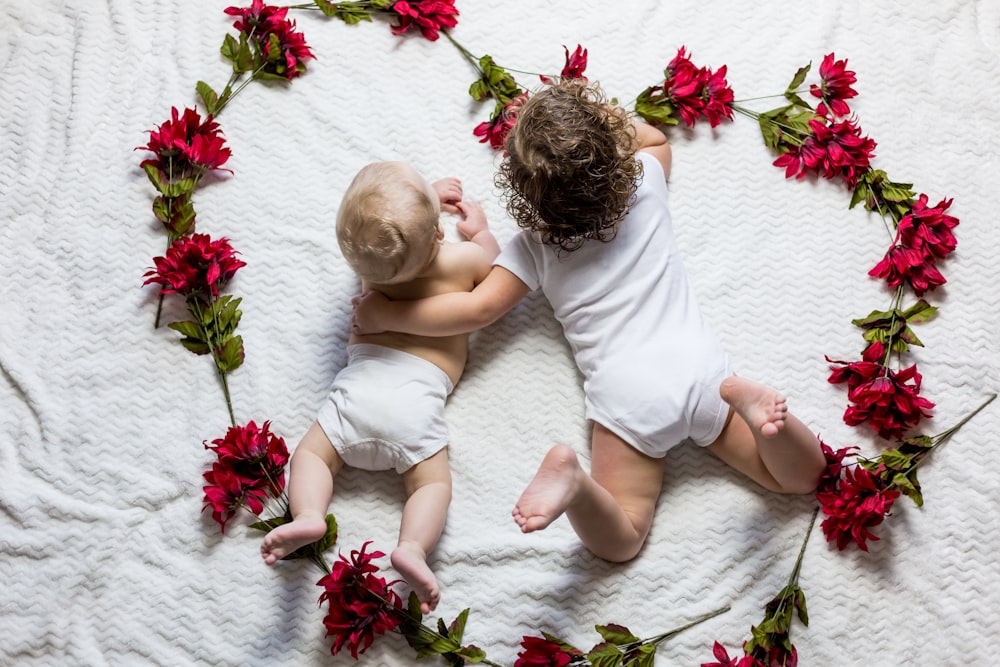 Due bambini sdraiati circondati da fiori dai petali rossi