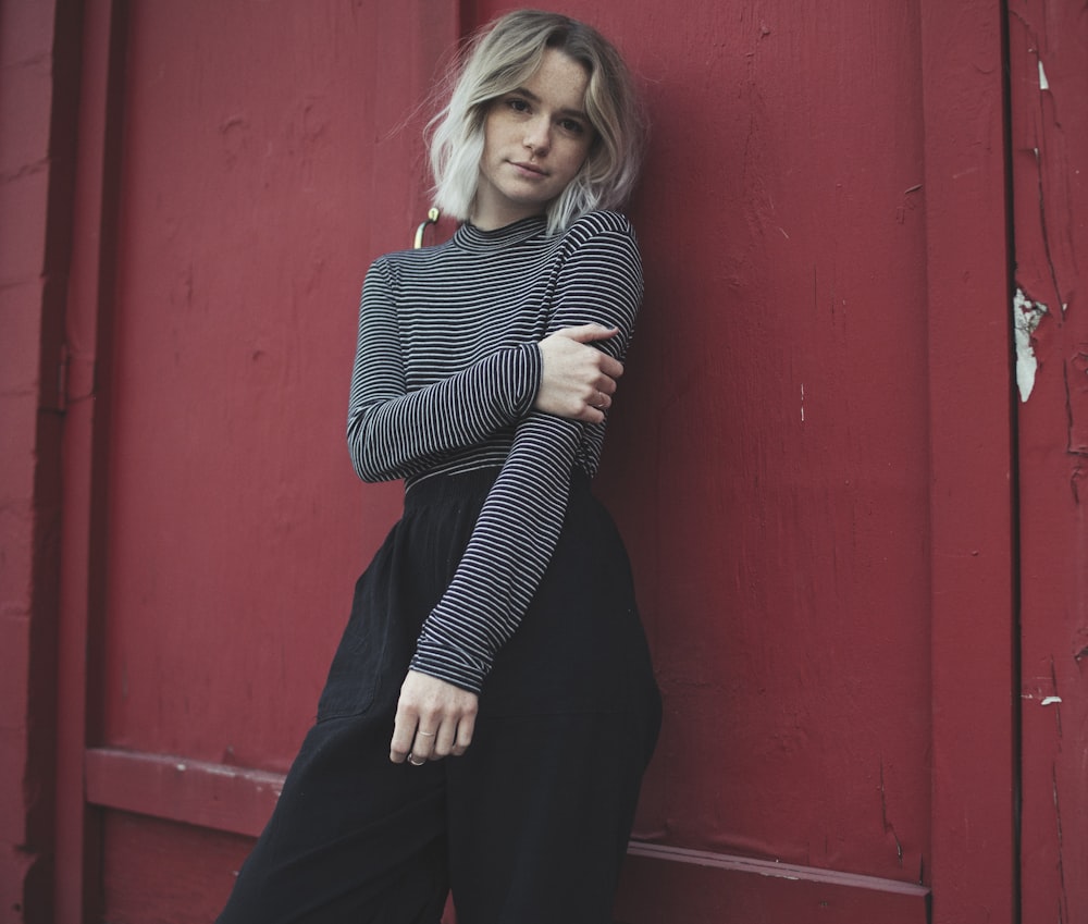 woman in gray top leaning her back on red wall