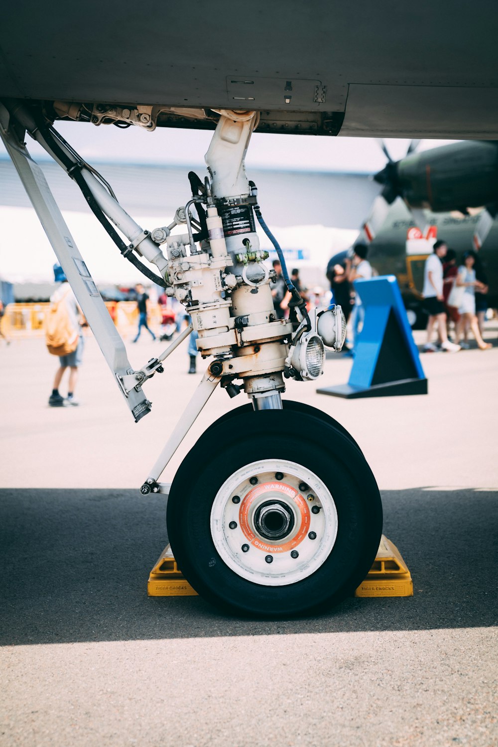 gray plane wheel on gray pavement with people gathered behind