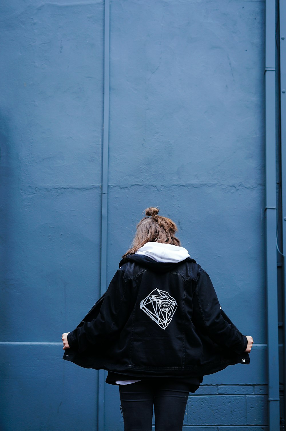 灰色の門の前に立つ黒いジャケットを着た女性