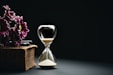 clear hour glass beside pink flowers