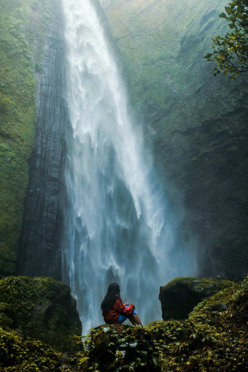 Donna che si siede sulle cascate di tuffo di fronte alla roccia