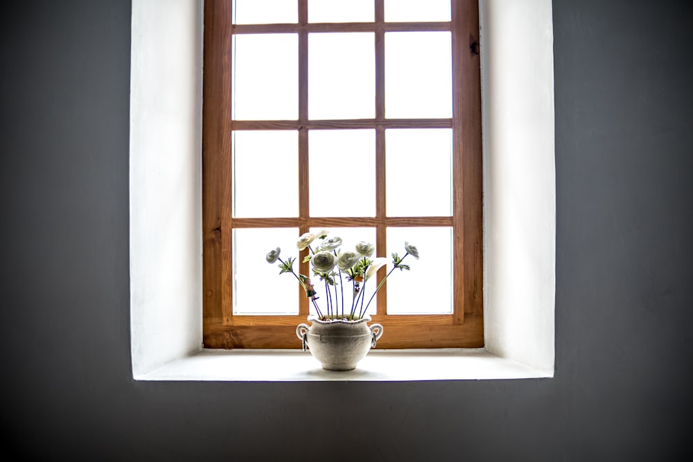 weiße Keramikvase mit weißen Blumen im Fenster bei Tag