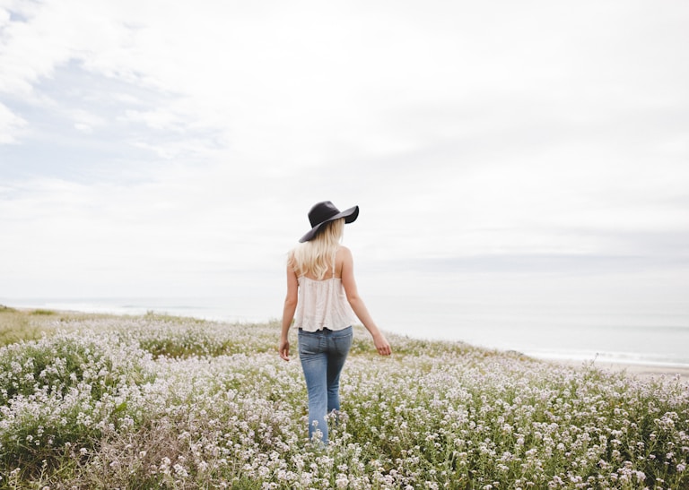 woman wearing black hat walking across the flower field during day time