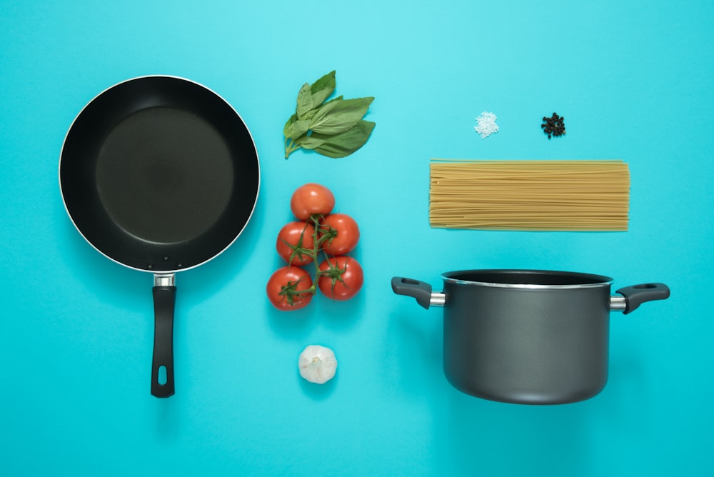flat lay photography of frying pan beside tomatoes on blue surface