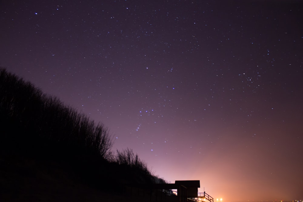 silhouette of shed on mountain under starry sky