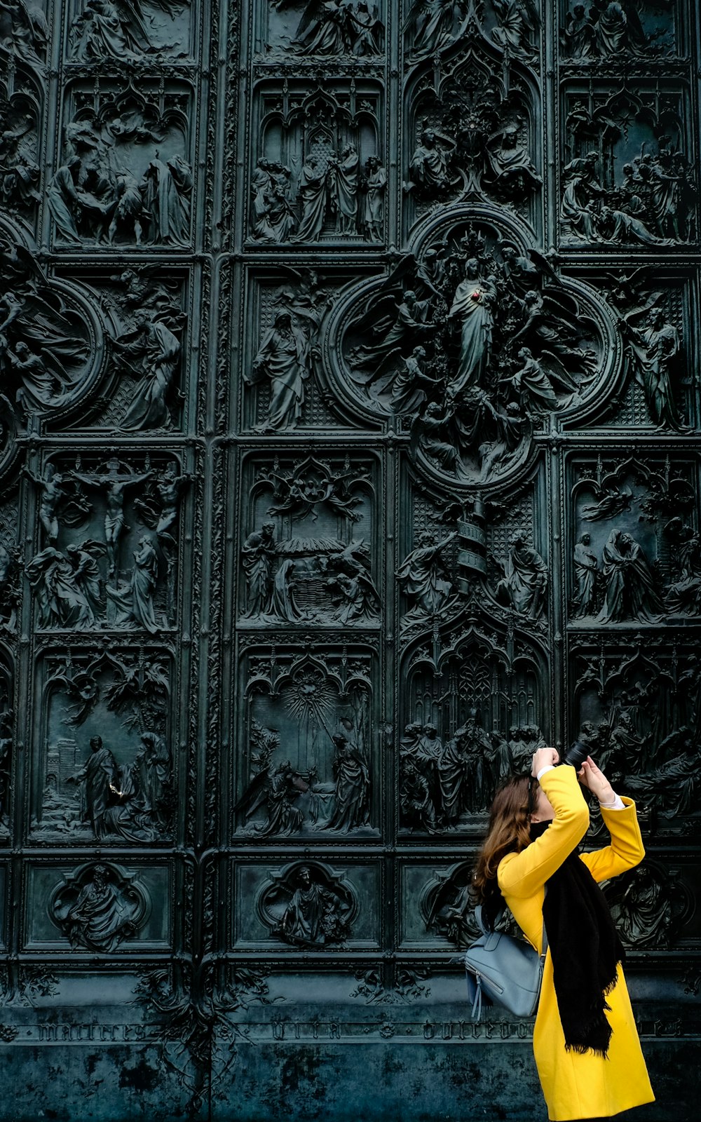 Mujer de pie tomando una foto con cámara frente a la pared del arte religioso