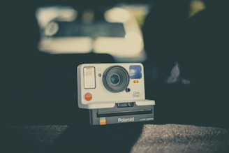 A vintage-style instant camera is centered against a blurred, dark background, displaying a classic design with a large lens and flash. The branding 'Polaroid OneStep 2' is visible on the front.