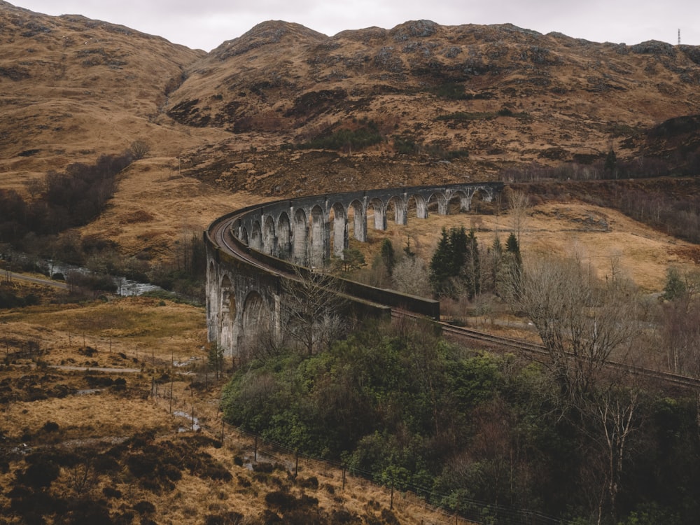 gray train rail bridge near mountain under white sky