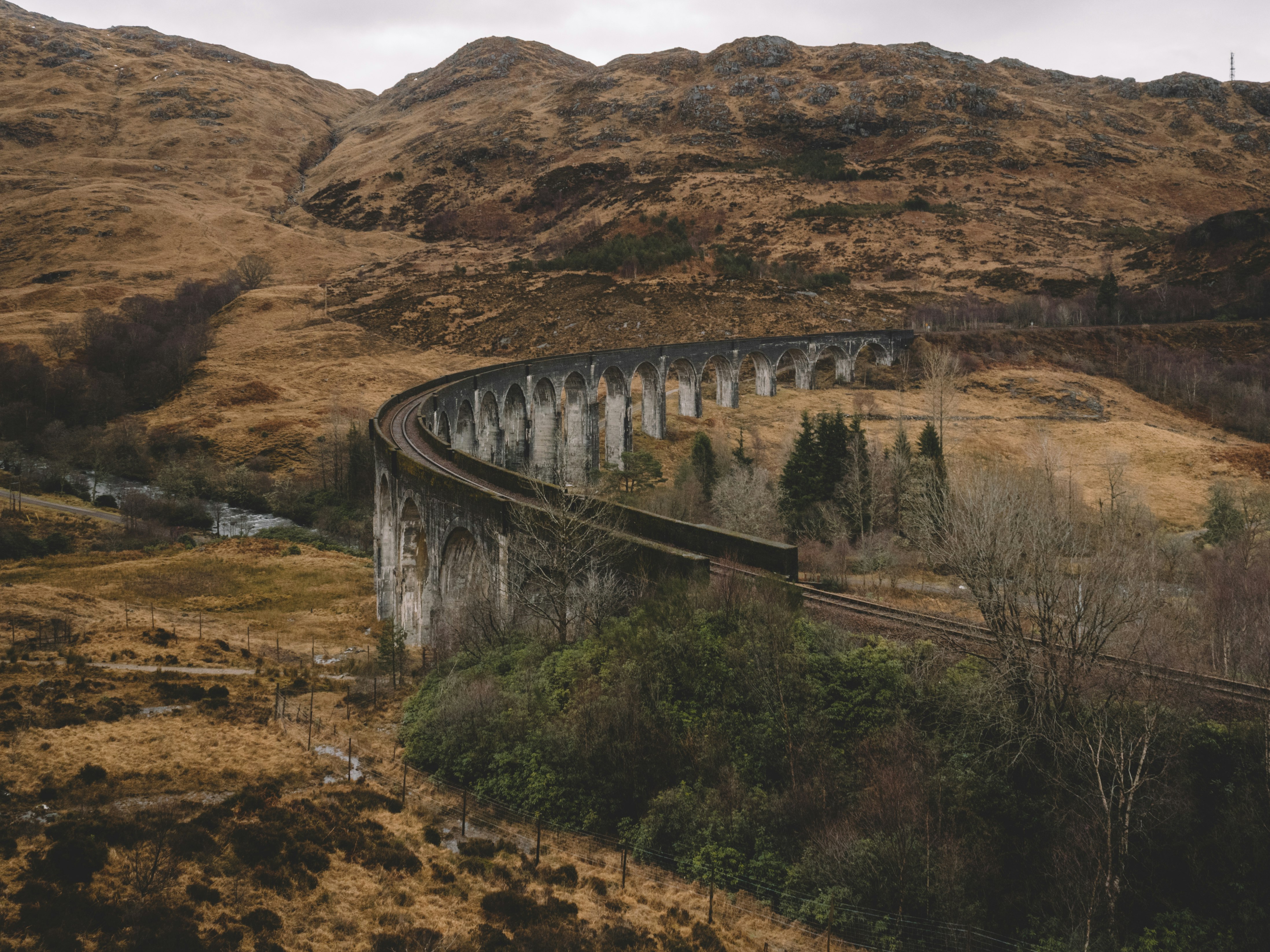 gray train rail bridge near mountain under white sky