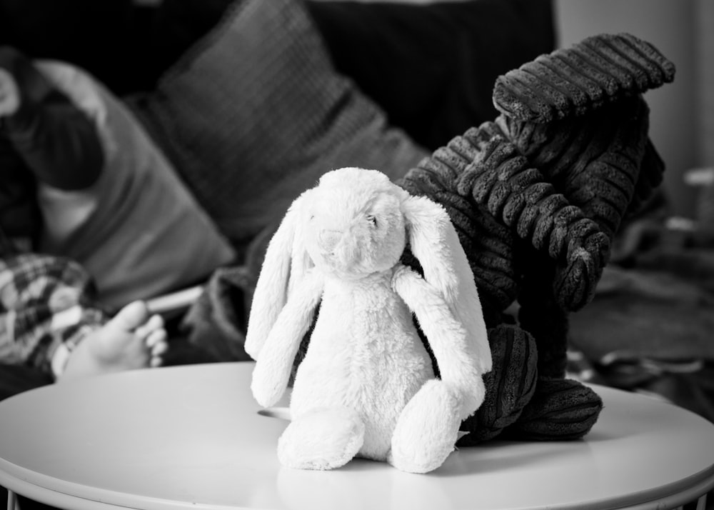 Photographie en niveaux de gris de deux jouets en peluche lapin sur le dessus d’une table basse