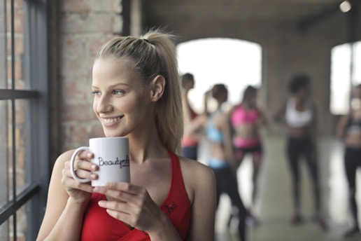 woman holding white ceramic mug while smiling near glass window