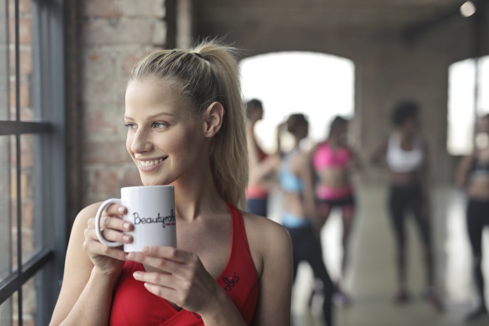 woman holding white ceramic mug while smiling near glass window
