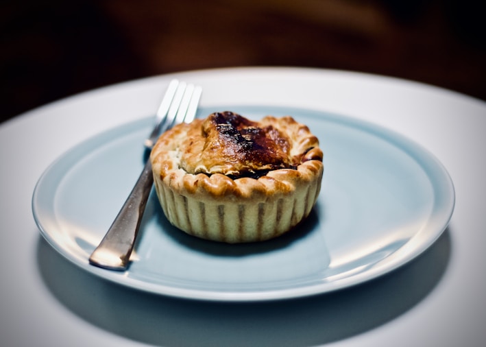 Close-up of a golden-brown British meat pie with flaky crust on a rustic wooden board