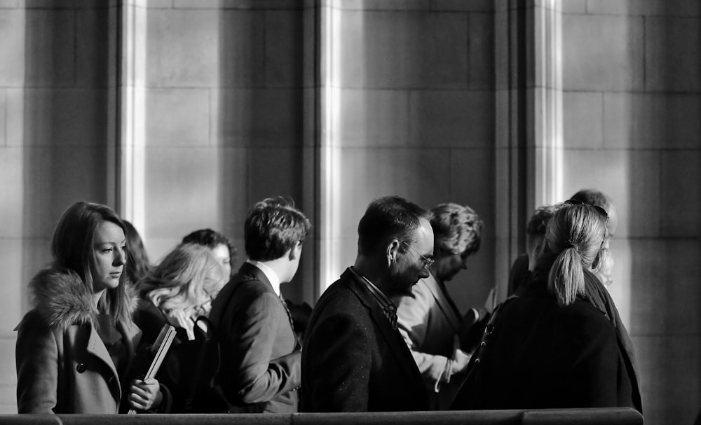 grayscale photography of men and women walking near wall