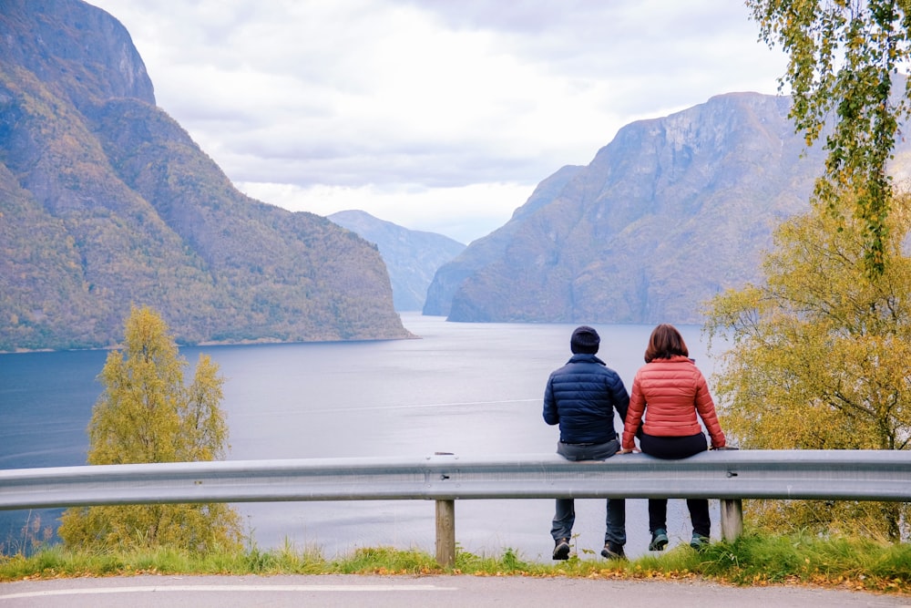 man and woman sitting on road fence