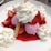 Scoops of pink ice cream topped with dollops of whipped cream and surrounded by fresh strawberries. A crispy wafer sticks out from one of the scoops. Strawberry syrup is poured over the dessert, pooling around the ice cream and fruit.
