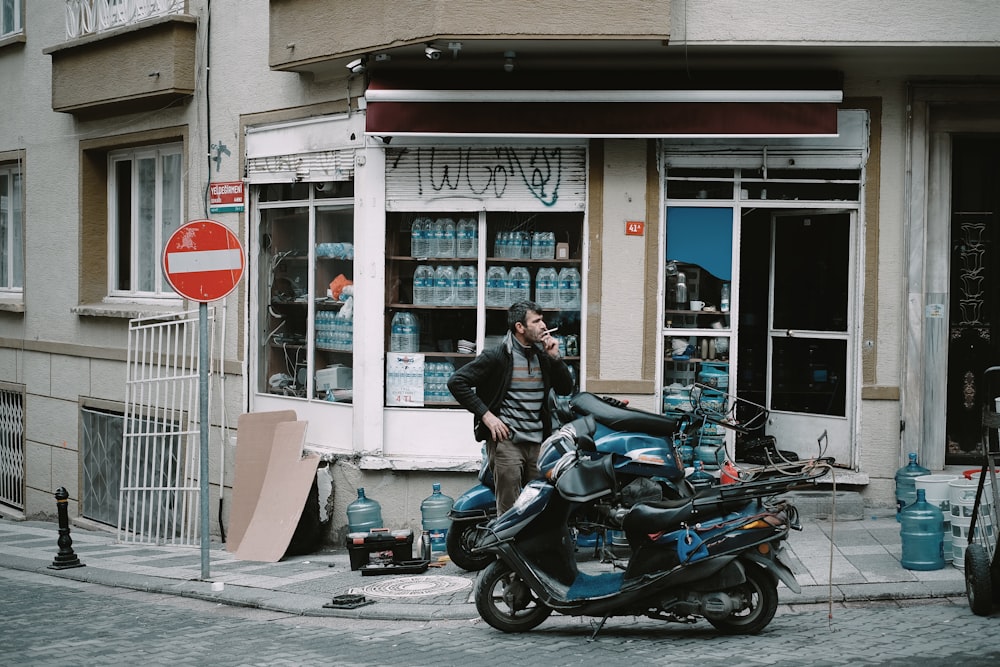 man standing near black and blue motor scooter on road