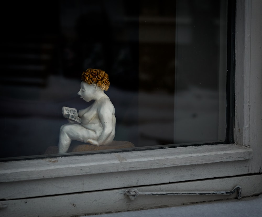 mujer leyendo la figurita del libro junto a la ventana