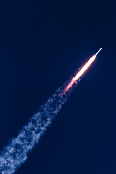 A rocket is ascending into the sky, leaving behind a fiery trail and plume of smoke against a deep blue background.