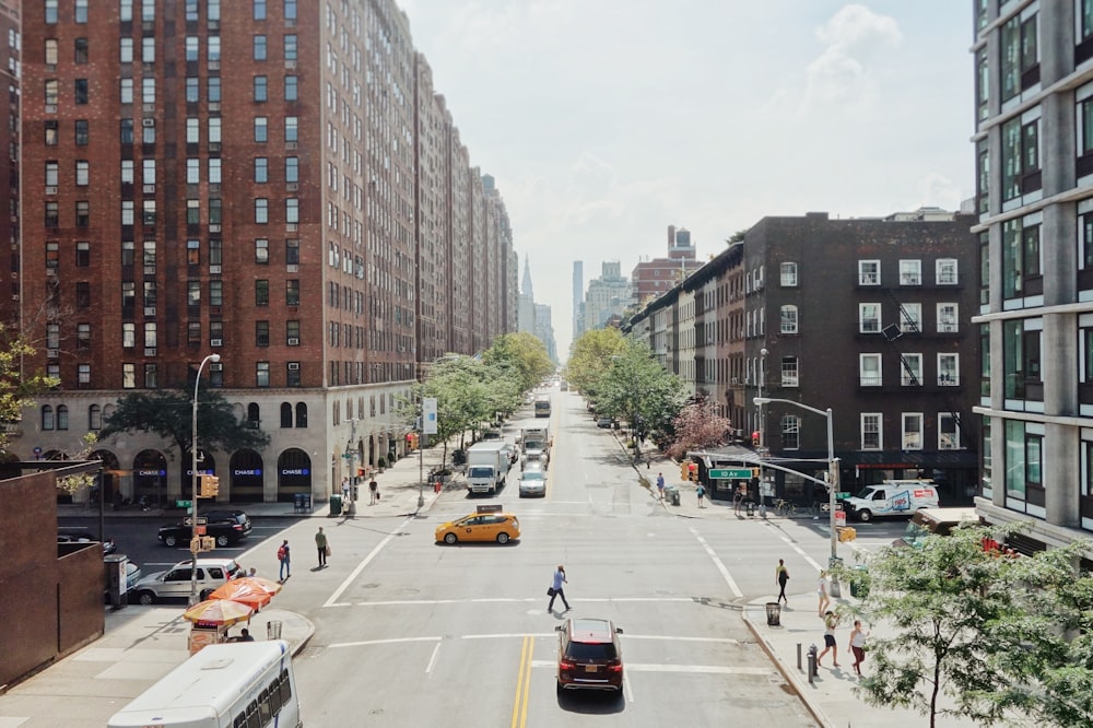 people walking on road beside cars between high rise buildings