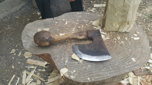 A rugged axe resting on a freshly split log beside a campfire.