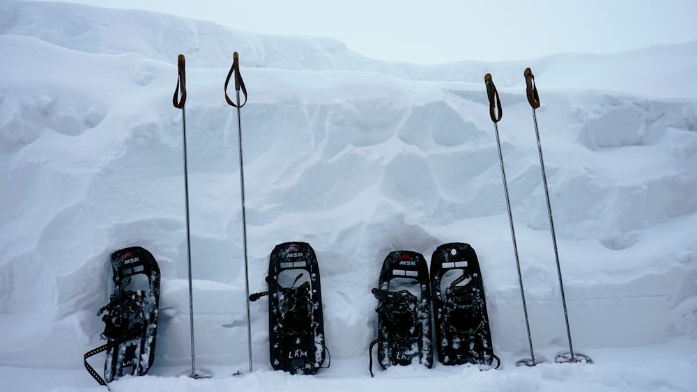 two pairs of snowshoes with poles leaning on snow