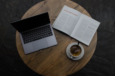 gray laptop beside white teacup and book