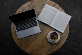 gray laptop beside white teacup and book