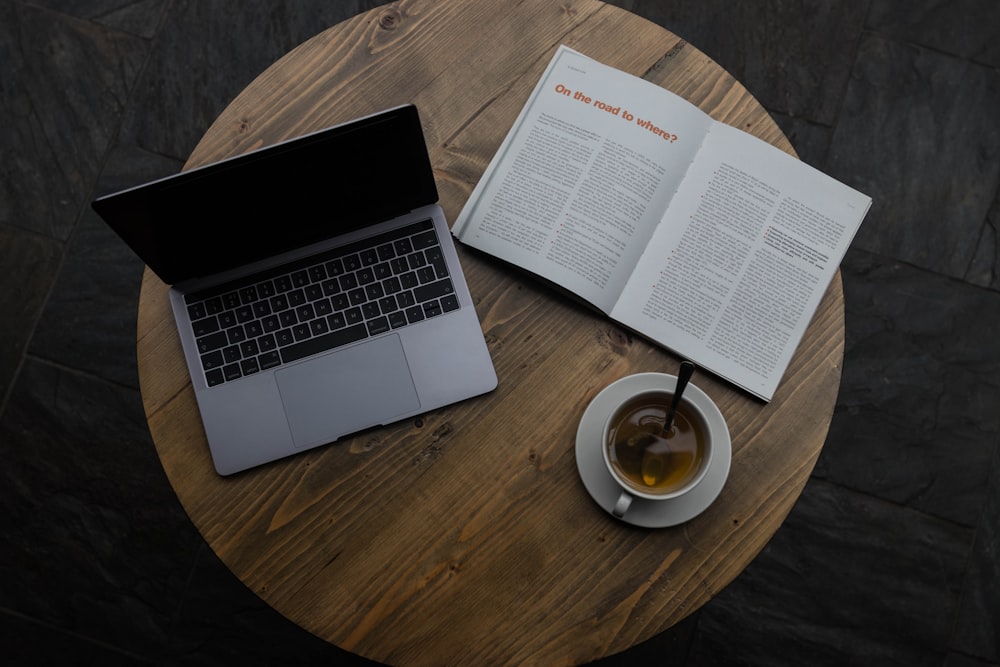 grauer Laptop neben weißer Teetasse und Buch