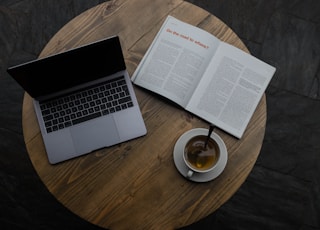 gray laptop beside white teacup and book