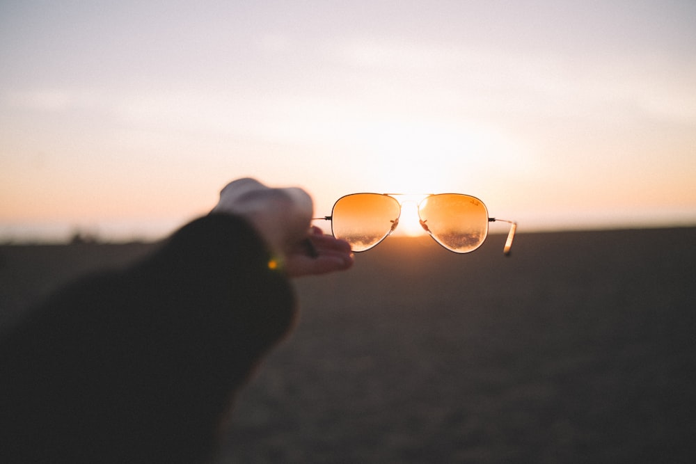 pessoa segurando óculos de sol marrom