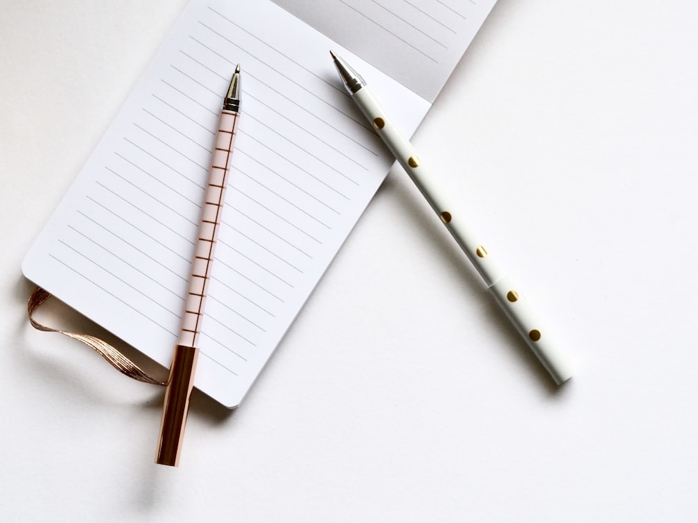 Dos bolígrafos blancos y beige sobre papel blanco