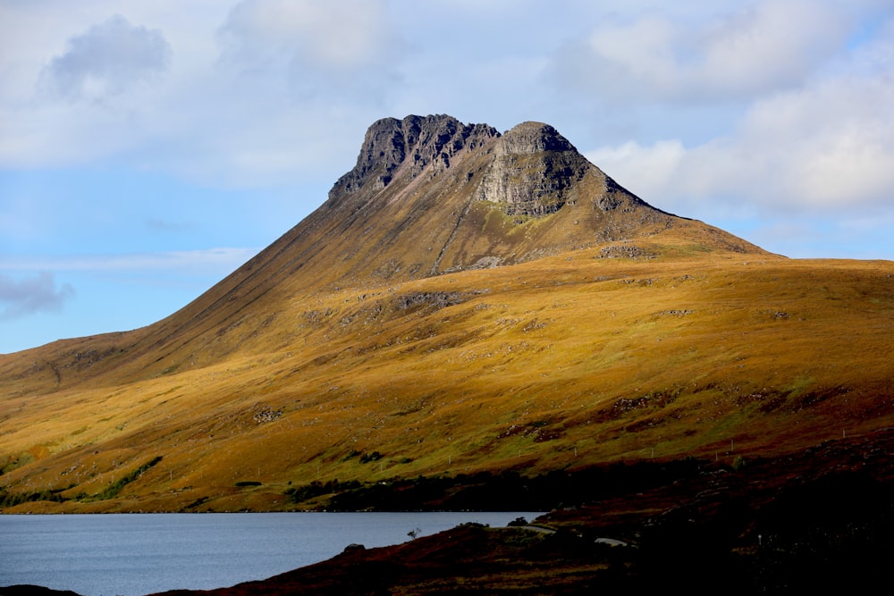 low-angle photography of brown mountain under cloudy sky