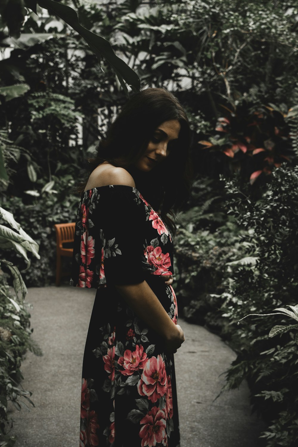 woman in black and red floral off-shoulder dress standing on pathway between green plants