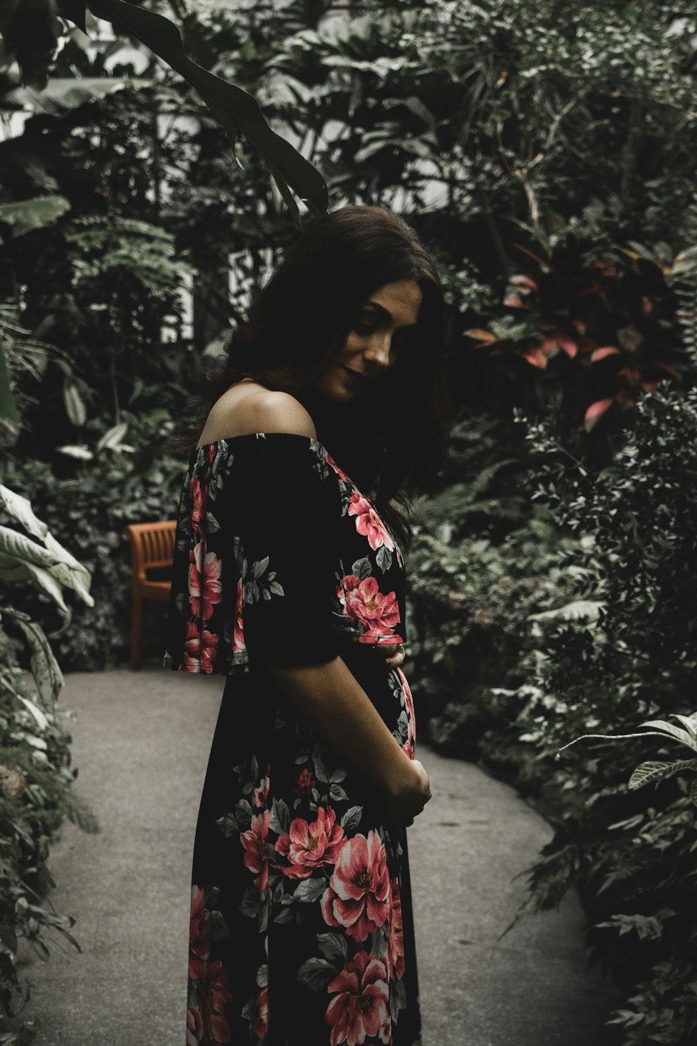 Mujer con vestido floral negro y rojo con hombros descubiertos de pie en el camino entre plantas verdes