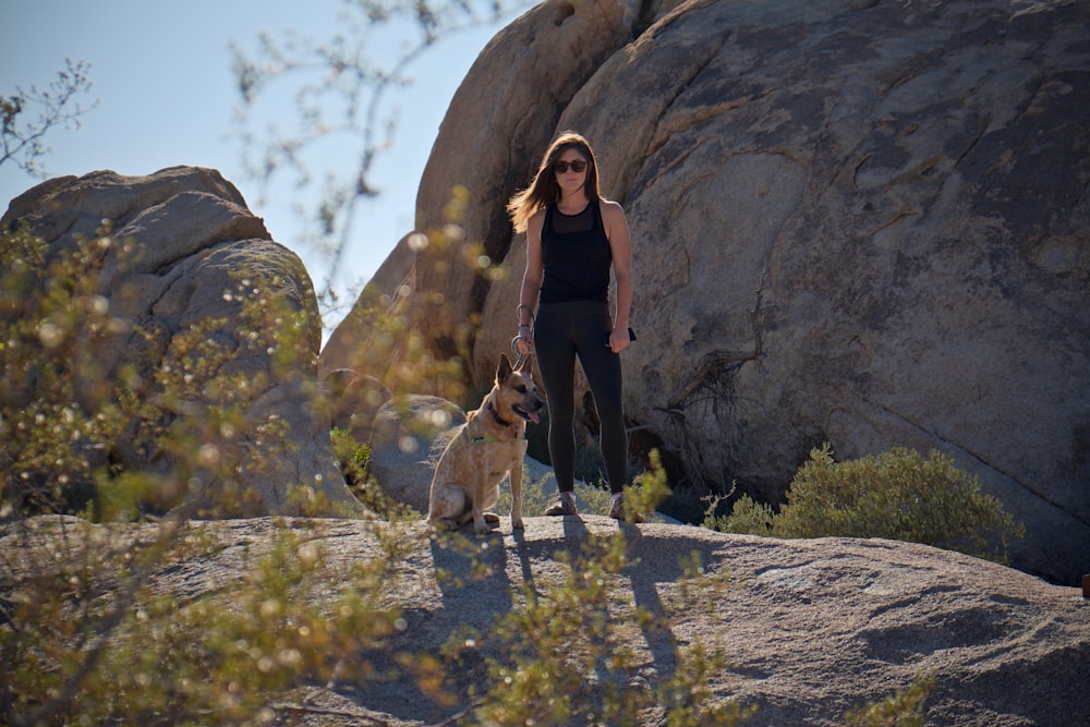 woman standing beside dog on rock
