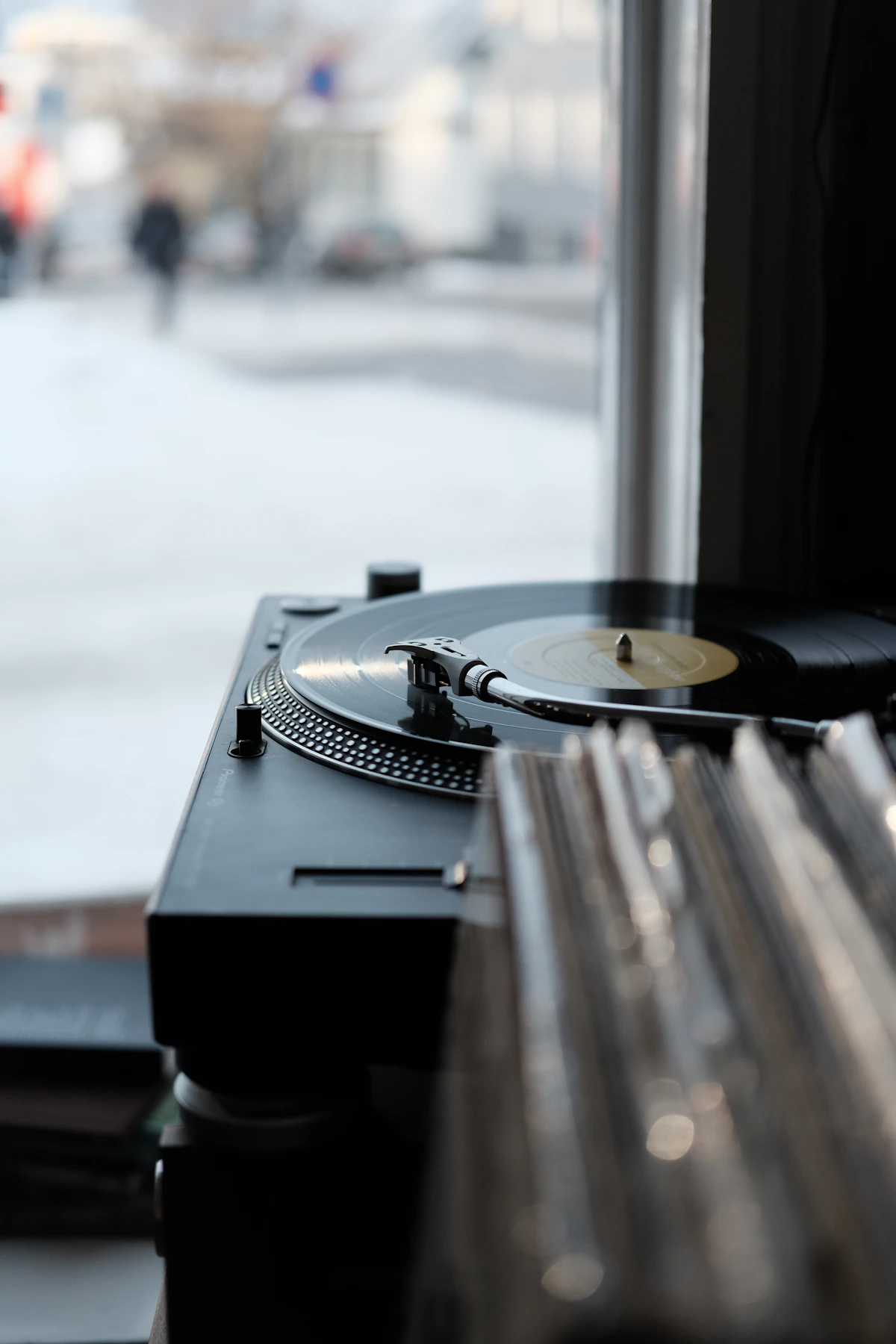 A turntable and stacked records in a dark room, one lamp catching the tonearm.